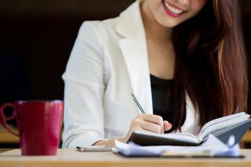 Business women writing something on her notebook close up.