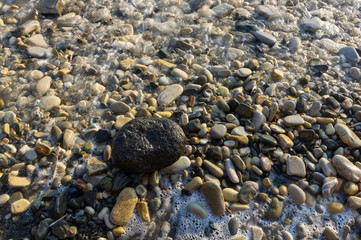 pebble stones on the sea beach, the rolling waves of the sea with foam