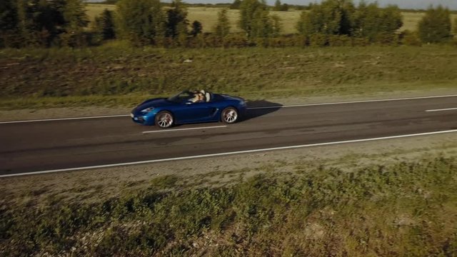 air survey blue sports car is on the road at sunset