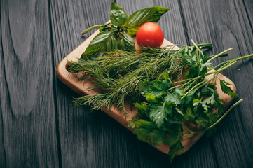 Tomatoes, parsley and dill on a wooden cutting board on a black wooden background. View of the sperm, place under the text.