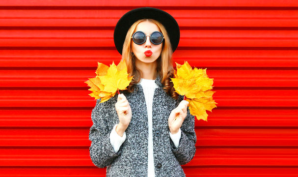 Happy cool girl with red lips holds yellow maple leaves on background