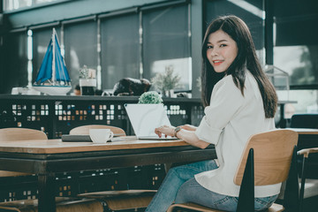 Obraz premium An Asian girl is freelancer woman, she is working by using the laptop computer and drinking a cup of coffee on morning in a coffee shop or her office.