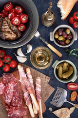 Italian antipasti wine snacks set. Brushettas, cheese variety, Mediterranean olives, pickles, Prosciutto di Parma with melon, salami and wine in glasses over black grunge background, top view