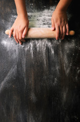 Girl hands keep rolling pin with flour on dark black table, baking background, top view, copy space...
