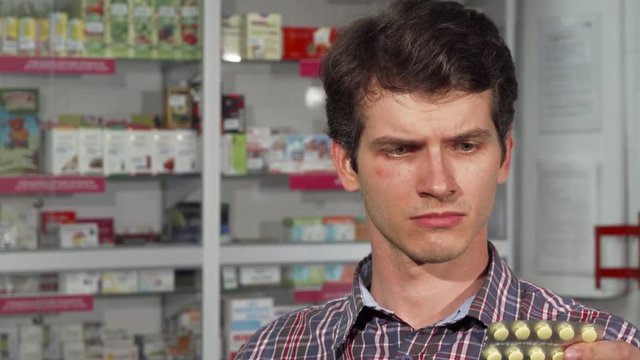 Attractive young man feeling sick, coughing while shopping for medications at the drugstore. Male customer with a flu looking for sore throat lozenges at the pharmacy. Remedy, medicine concept.