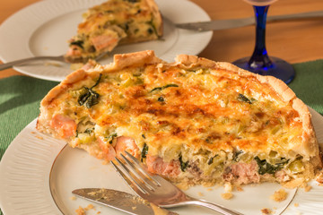 Closeup of spinach pie slices with salmon, onions, celery stalks and cheese on plates 