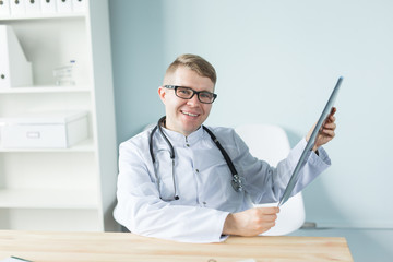 Healthcare, medical and people concept - Smiling doctor sitting holding radiograph in his hands