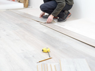 DIY, repair, building and home concept - close up of male hands lying parquet floor board/laminate flooring