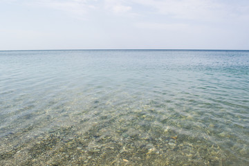 Clear and quiet sea water with stones and blue sky with clouds.