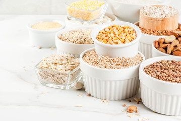 Selection various types cereal grains groats  in different bowl on white marble background, copy space