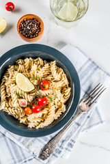Classic italian pasta fusilli with pesto sauce, tomatoes, lime and fresh herbs in dark bowl, white...
