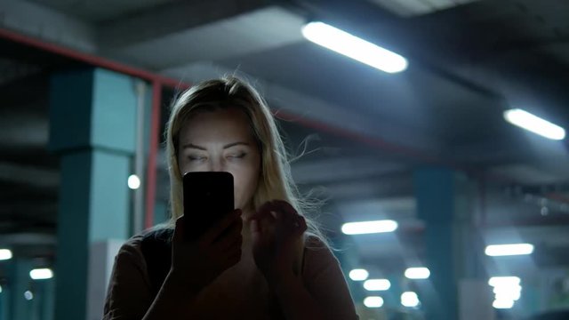 Blond woman shocked and watched mobile phone at dark parking place