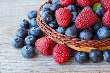 Freshly picked organic raspberries and blueberries in a basket on old wooden background.Blueberry and raspberry.
Healthy eating,summer fruits or diet concept.Selective focus.
