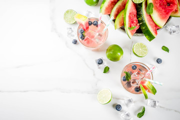 Summer refreshment drink, watermelon and blueberry lemonade cocktail with lime, mint and ice cubes, white marble background copy space top view