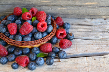 Freshly picked organic raspberries and blueberries in a basket on old wooden background.Blueberry and raspberry.
Healthy eating,summer fruits or diet concept.Selective focus.