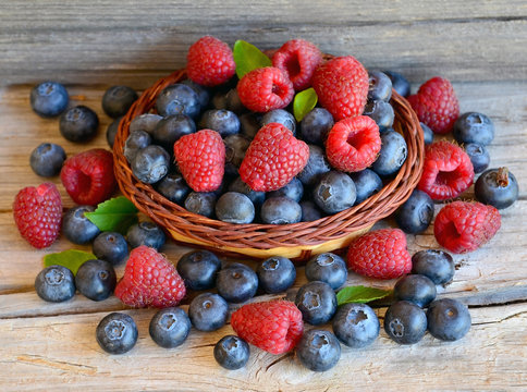 Freshly picked organic raspberries and blueberries in a basket on old wooden background.Blueberry and raspberry.
Healthy eating,summer fruits or diet concept.Selective focus.