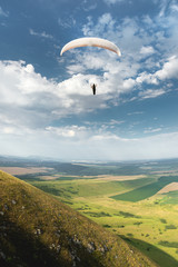 White orange paraglide with a paraglider in a cocoon against the background of fields of the sky and clouds. Paragliding Sports