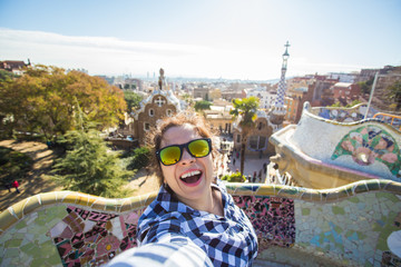 Fototapeta premium Young happy woman making selfie portrait with smartphone in Park Guell, Barcelona, Spain