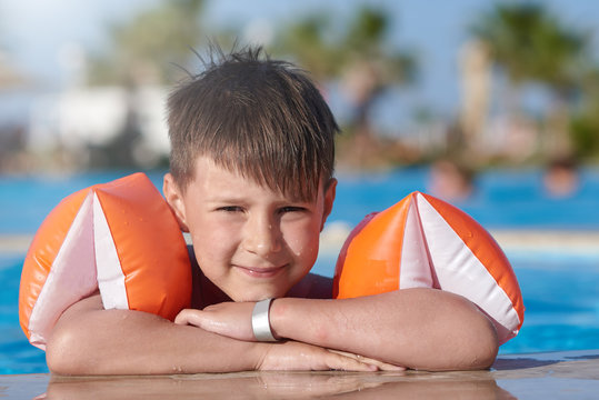 Portrait of smiling Caucasian boy in floating sleeves spending time in pool at resort.