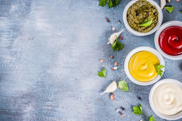 Set of four classic sauces - ketchup, mayonnaise, mustard, pesto - with herbs and spices. Blue concrete background top view copy space