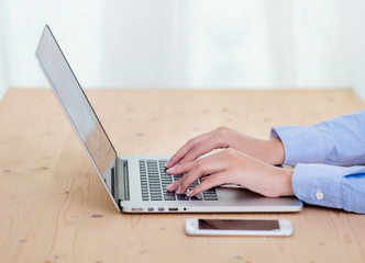Fototapeta premium Woman hands typing on laptop keyboard at the office, Woman worker and business concept, Soft focus on vintage wooden table.