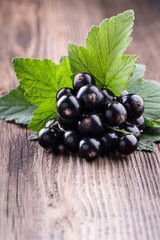 Fresh ripe black currant with original leaves on old wooden background close-up