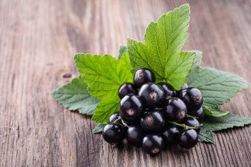 Fresh ripe black currant with original leaves on old wooden background close-up