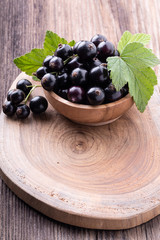Fresh ripe black currant in wooden bowl with original leaves on rustic old background