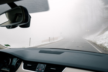 Driver point of view pov at the lonely road running away among slope with snow in thick fog - winter security driving