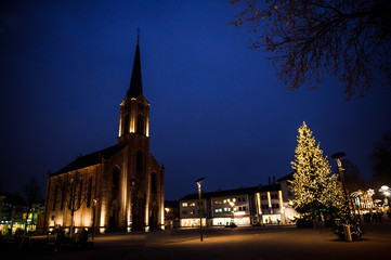 Calm City with illuminated german evangelical church during the winter Christmas holidays in central Kehl, Baden-Wurttemberg, Germany with Christmas Tree and pedestrians silhouettes
