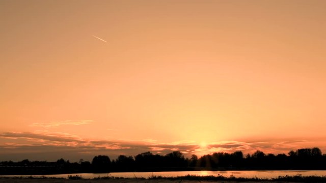 A teenager in a white T-shirt on a bicycle rides past a river or lake early in the morning at dawn. Silhouette of a bicyclist on a background of a golden sky before sunrise. Sports lifestyle.