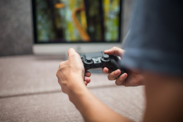 a young man is playing with a joystick on the game console on a background of a blurry monitor © silentalex88