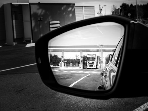Car rear view mirror with reflection of white truck filling gas at the gas station - black and white image