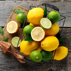 Top view of lemons and limes fruits in basket on wooden background.