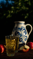 Traditional apple wine in the city of Frankfurt in Hesse. A jug of wine is on an old wooden table in the garden, around it are apples