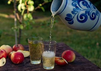 a man's hand pours Traditional apple wine in a refilled glass in the city of Frankfurt. A jug of wine on an old wooden table in the garden, around it apples