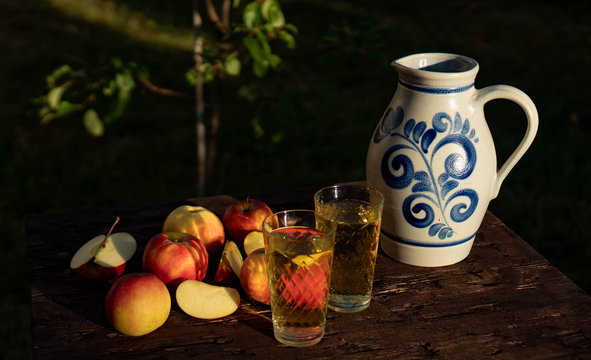 Traditional apple wine in the city of Frankfurt in Hesse. A jug of wine is on an old wooden table in the garden, around it are apples