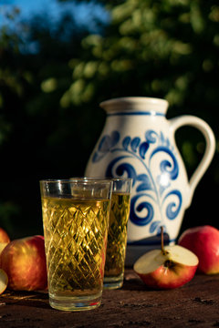 Traditional apple wine in the city of Frankfurt in Hesse. A jug of wine is on an old wooden table in the garden, around it are apples