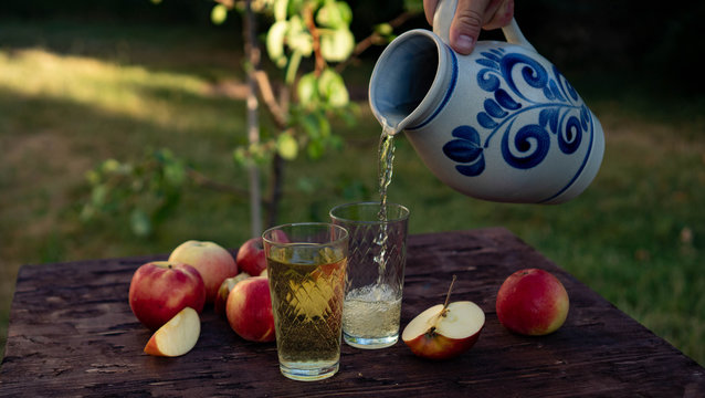 a man's hand pours Traditional apple wine in a refilled glass in the city of Frankfurt. A jug of wine on an old wooden table in the garden, around it apples