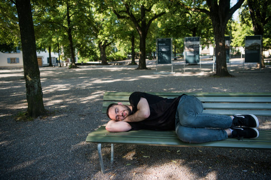 Poor homeless man sleeping on the wooden bench at park