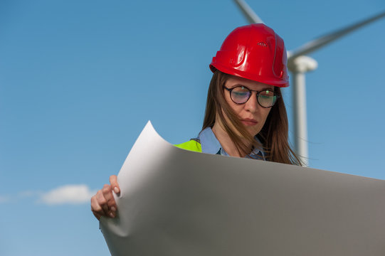 Serious young woman engineer looking at a plan of repair work on the background of a windmill