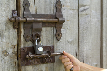 Close-up of lit by sun old rough made of wooden planks house door or barn gate with iron rusty...