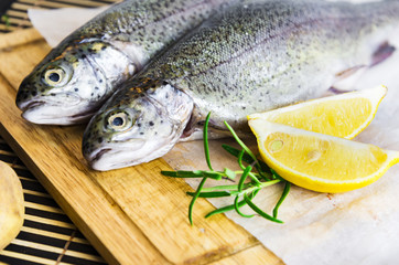 A table with a cutting board with fresh trout, slices of lemon and rosemary on the side
