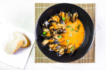 Delicious seafood mussels with red sauce, baguette and green onions