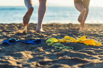 Female and male legs with bikini and swimming trunks on the sand on a sunset background. Concept