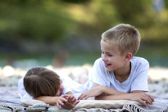 Two young happy cute blond laughing children, boy and girl, brother and sister having fun on pebbled beach on blurred bright sunny summer bokeh background. Friendship and perfect holiday concept.