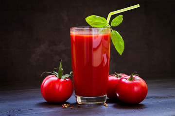 Ripe fresh red tomatoes and a glass of tomato juice in a glass transparent glass, spices, basil....