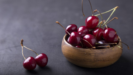 Fresh ripe cherries in a round wooden bowl with copy space on dark background