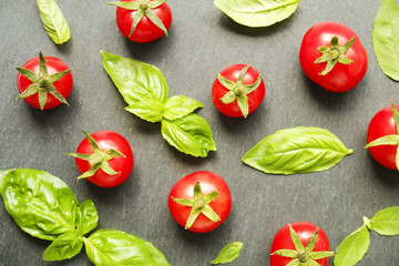 Bunch of juicy organic red cherry tomatoes arranged with green basil leaves on black slate stone background. Polished vegetables. Clean eating concept. Vegetarian diet. Copy space, flat lay, top view.