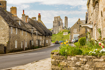 Corfe castle ruins in Dorset seen on a sunny summer day with traditional portland stone cottages lining the road in the foreground - obrazy, fototapety, plakaty